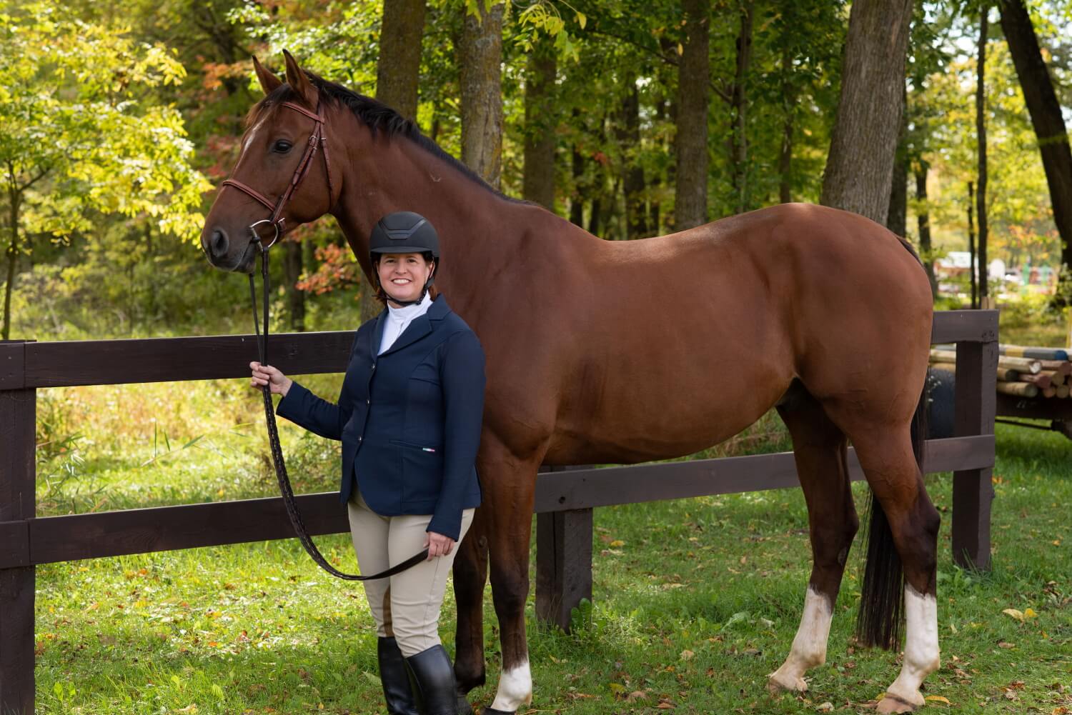 Andrea holding a Dutch Warmblood (Beckett) by the reins in a sunny Midwestern grove