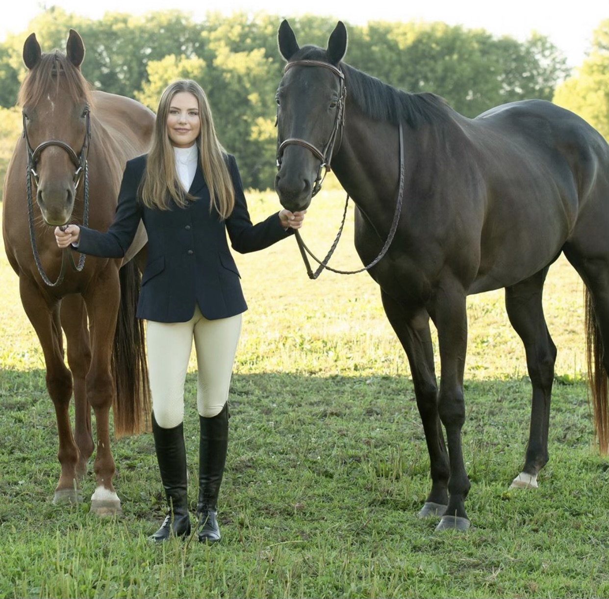 Young lady in an English style uniform holding two Thoroughbred horses by the reins